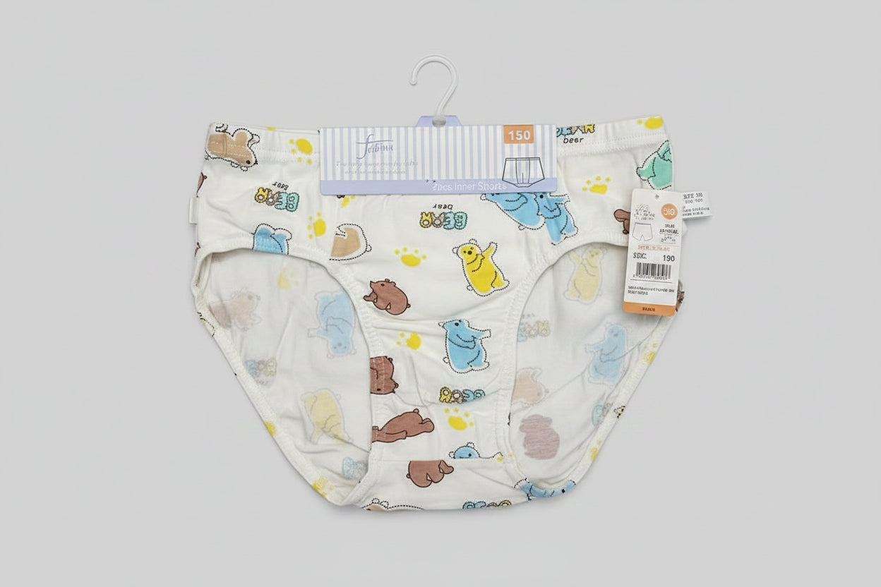 A pair of white baby underwear with a colorful cartoon animal print, laid flat on a light wood surface next to a plastic measuring ruler.