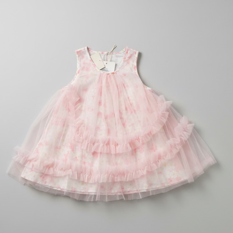 A sleeveless tiered tulle dress for a toddler girl, featuring a light pink and white floral pattern, laid flat on a dark wood surface.