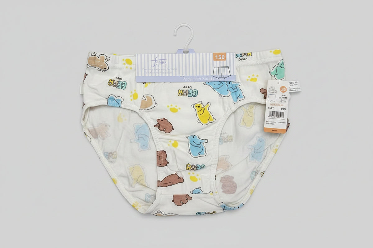 A pair of white baby underwear with a colorful cartoon animal print, laid flat on a light wood surface next to a plastic measuring ruler.