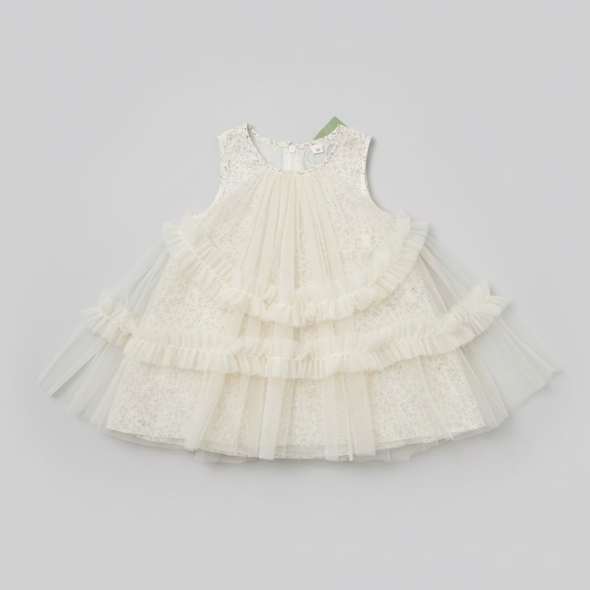 A sleeveless white tulle dress with a delicate floral lace bodice and layered ruffles, laid flat on a dark wooden table.