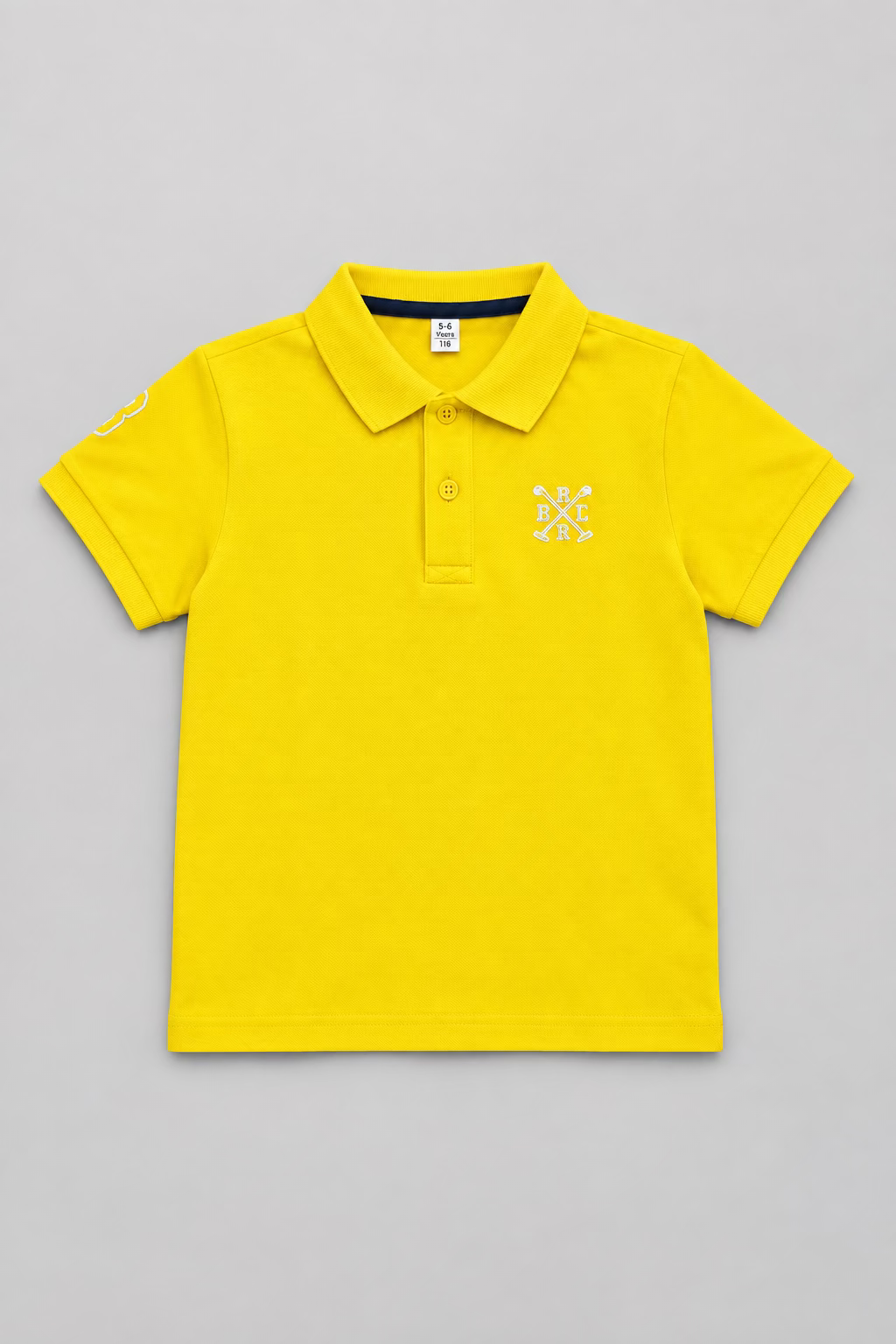 A bright yellow short-sleeve polo shirt laid flat on top of a brown cardboard box. The shirt has a small white embroidered logo on the left chest and a black-and-white neck label, with a small hangtag attached near the collar.